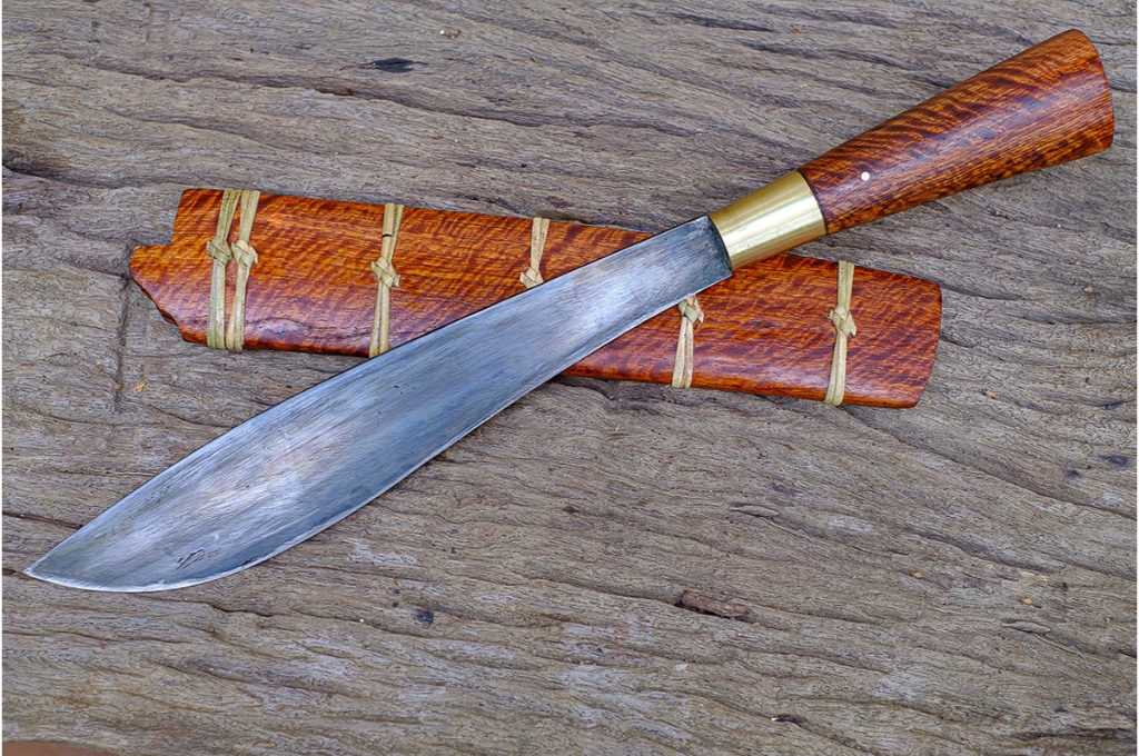 couteau avec un étui en bois pour le ranger. son manche est en bois. ils sont posés sur une table en bois.