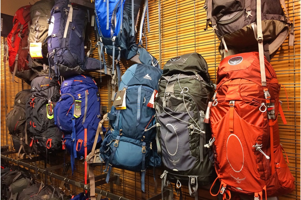 dans une boutique, sont accrochés une multitude de sacs à dos de randonnée de diverses couleurs de la marque Osprey.