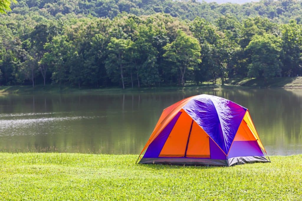une tente orange et bleu est posée près d'un lac autour d'une forêt luxuriante.