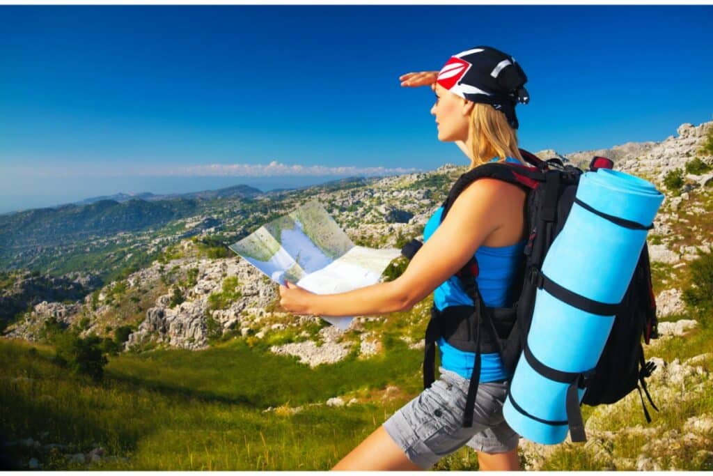 une femme en randonnée tient une carte de randonnée et regardant le paysage au loin. elle porte un sac à dos avec un tapis de sol bleu.