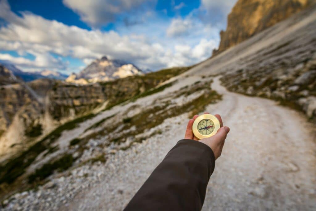 une personne tient à bout de bras une boussole sur un chemin de randonnée en montagne