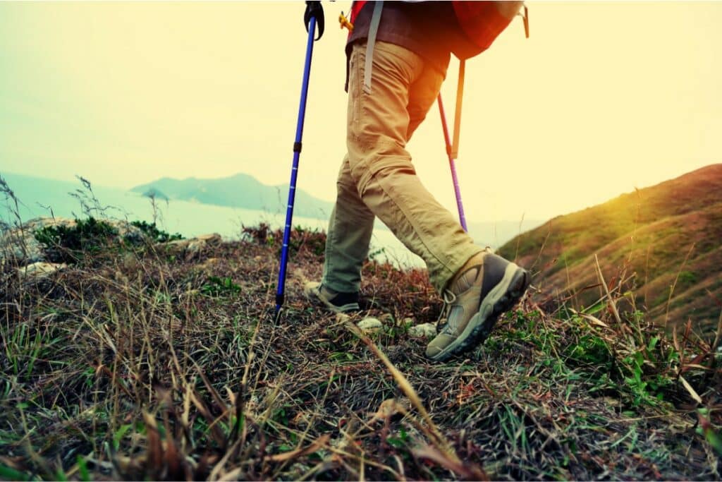 un randonneur avec des bâtons de marche parcourt la montagne. il porte un sac à dos de randonnée, un pantalon beige et des chaussures de rando.