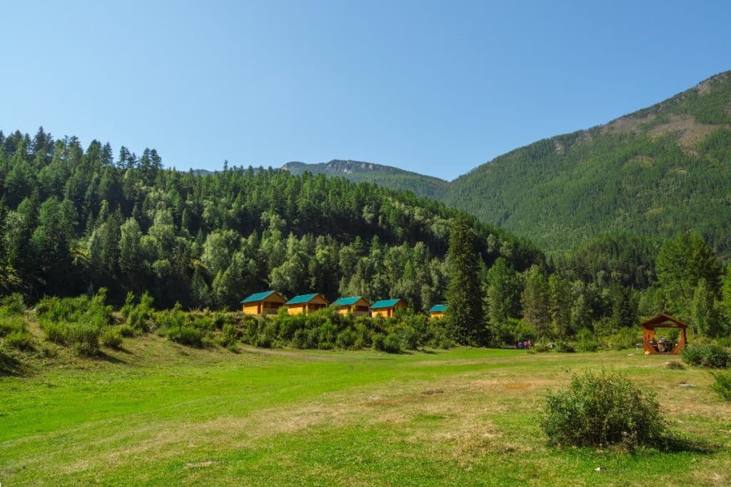 6 astuces pour pratiquer une randonnée éco responsable Conseils randonnée collective camping with green lawn in an ecofriendly green place summer tourist complex wooden guest houses against the background of fircovered high mountains