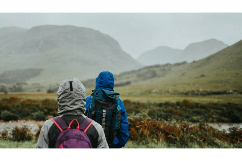 2 personnes en randonnée en habit de pluie avec une capuche et portant un sac à dos, regarde le paysage de montagne dans une légère brume